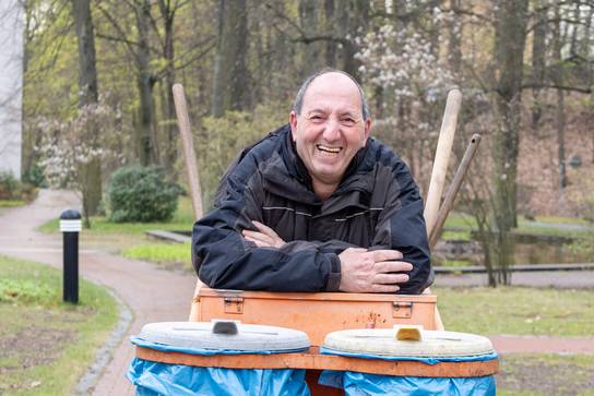 Zu sehen ist ein älterer Mann, der sich auf einen Wagen mit Mülleimern auflehnt. 